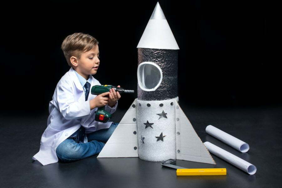 Little boy in white coat drilling toy rocket with toy drill Reach Out Into Space